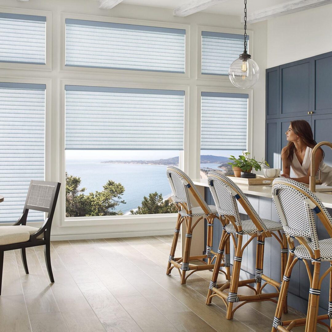 A woman sitting at the table in front of windows.