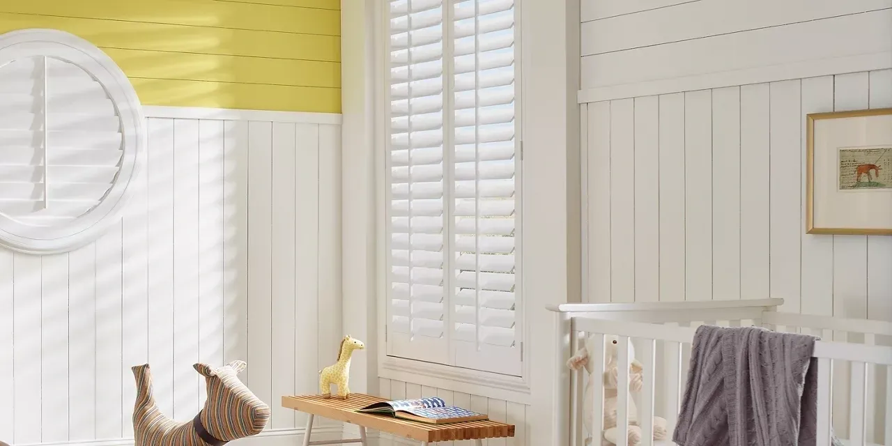 A baby 's room with yellow walls and white shutters.