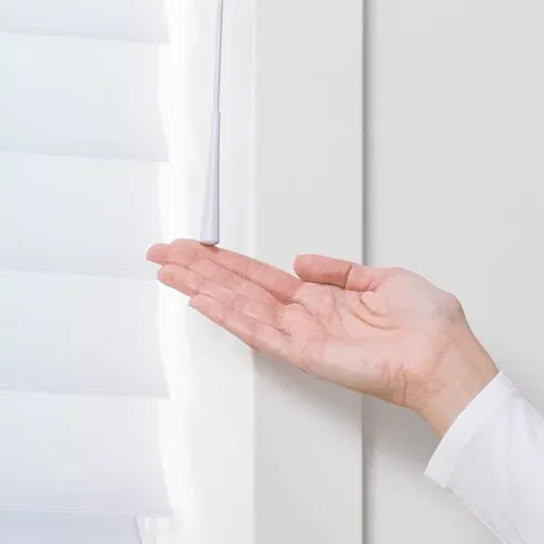 A person 's hand is reaching out to touch the blinds.